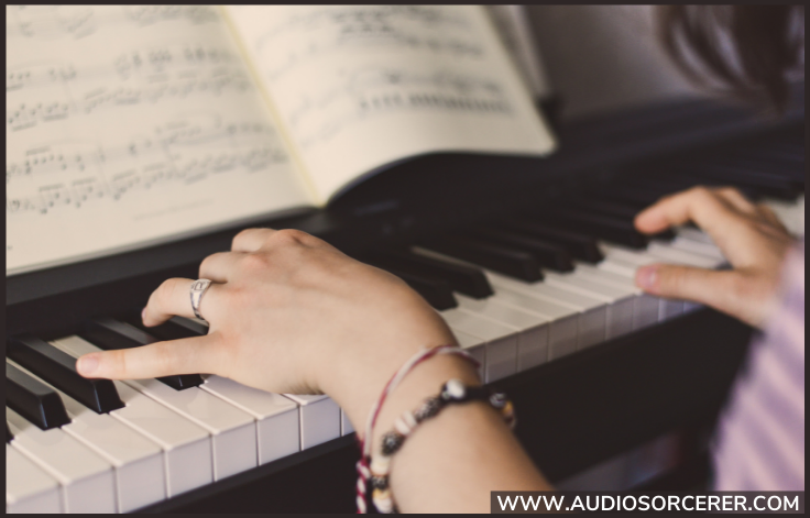 Closeup of hands playing a keyboard with sheet music visible.