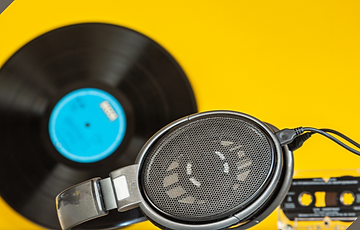 Open-back headphones with a record and tape cassette on a yellow background.