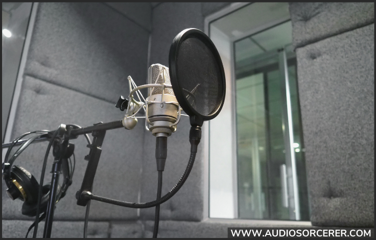 A condenser microphone on a stand with a nylon pop filter in front of it in a vocal booth.