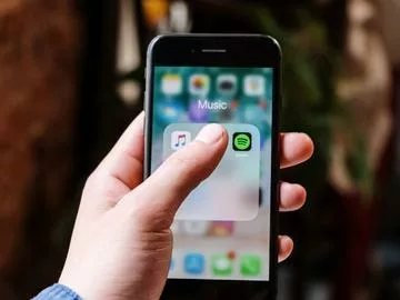 A hand holding a phone showing the icons for Apple Music and Spotify.