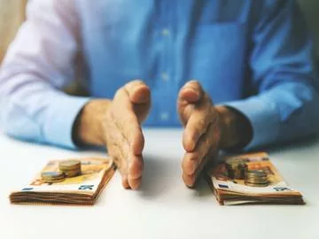 A person sitting a table splitting money into two separate piles.