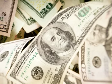 A bunch of money with a 100 dollar bill in the forefront.