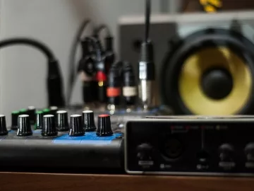 A mixing board, audio interface, and a studio monitor on a table.