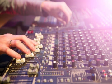 Closeup of an audio engineer adjusting faders and knobs on a mixing console.