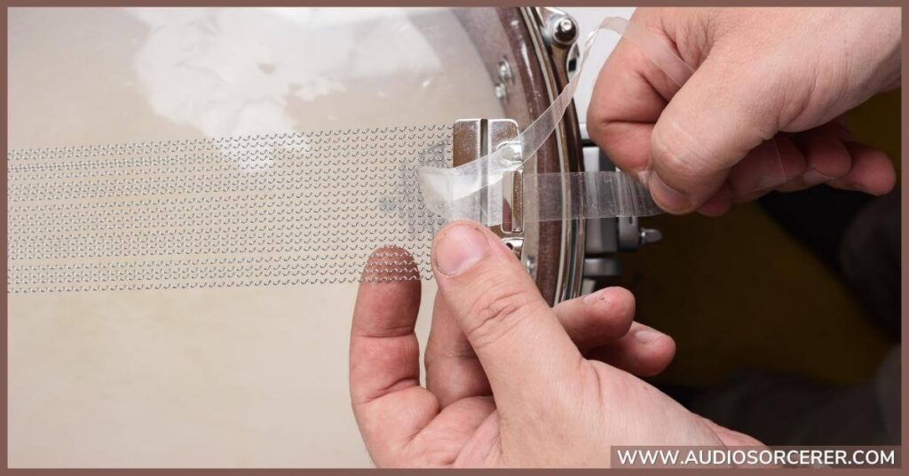 A closeup of a man adjusting the wires on a snare drum.