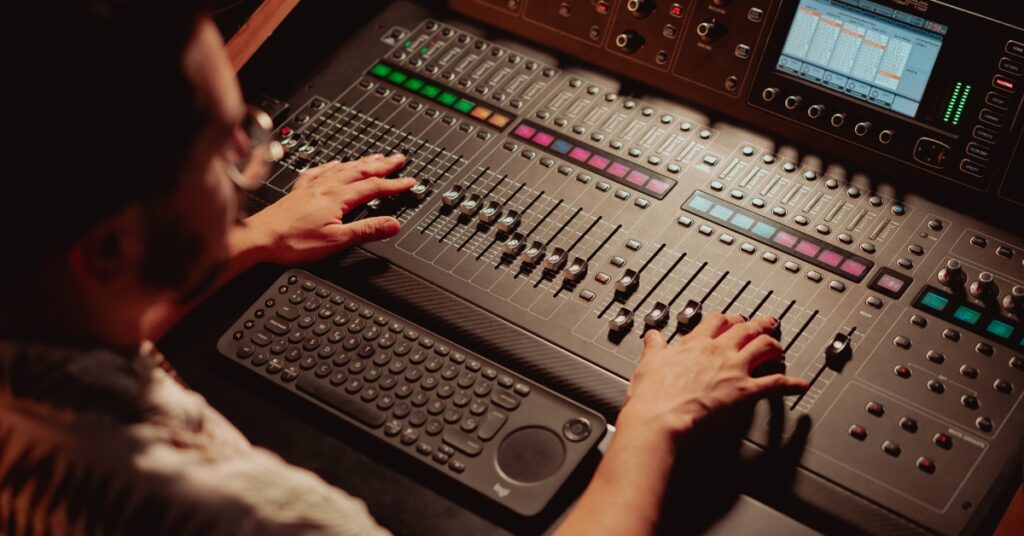 Closeup of an audio engineer moving faders on a mixing console.